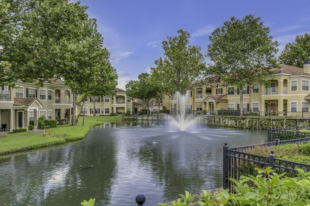 A fountain in the middle of a pond in front of apartment buildings.