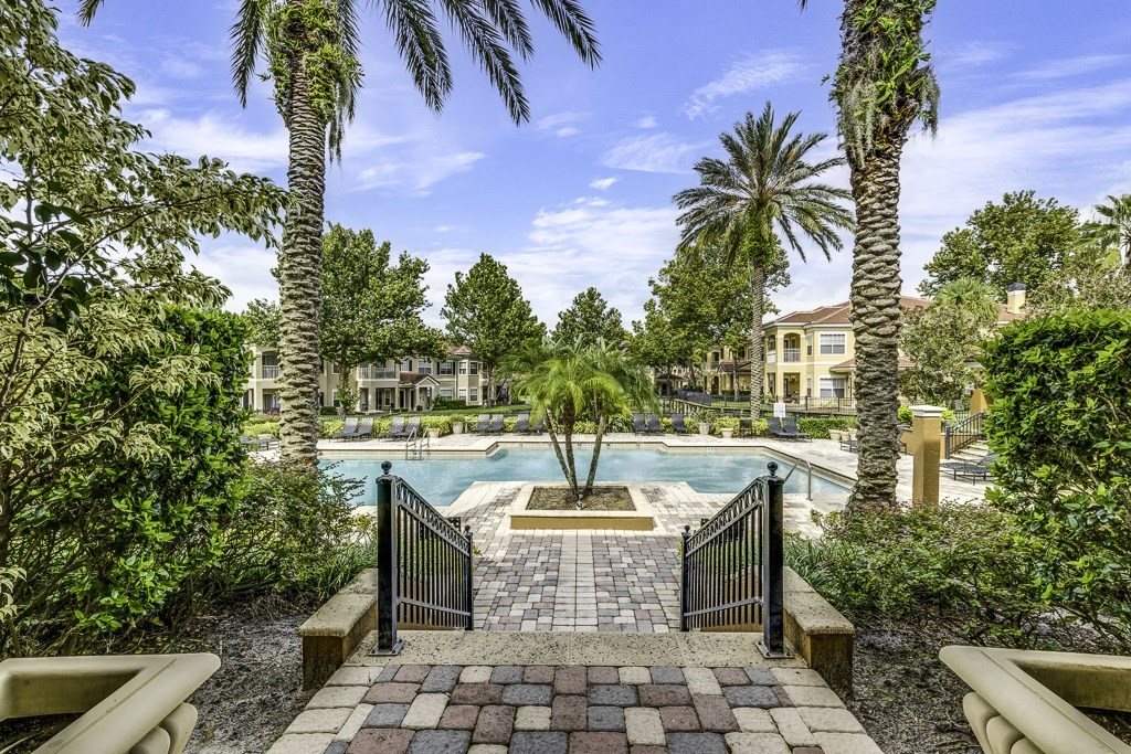A pool surrounded by palm trees and a brick walkway.