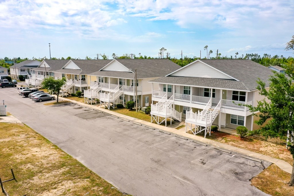 A row of houses with white balconies and a parking lot in front.