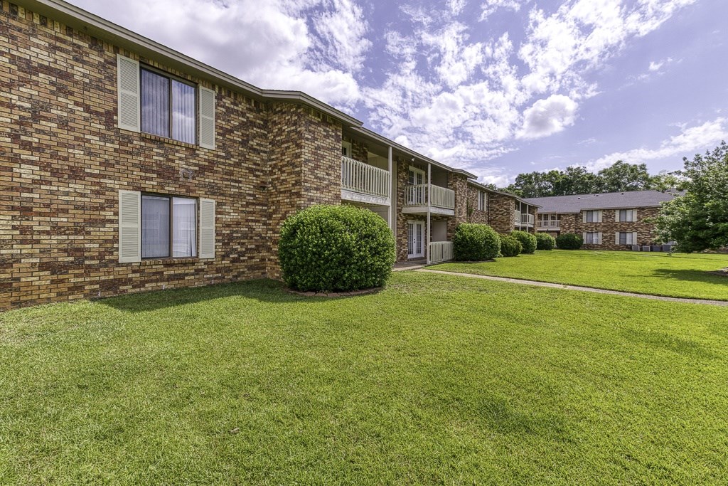 A grassy area in front of a brick building with a cloudy sky above.