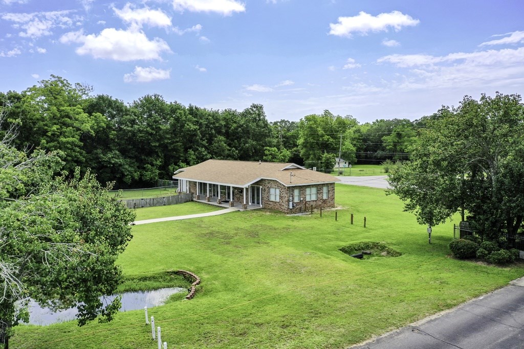 A house with a brown roof is surrounded by a green lawn and trees.