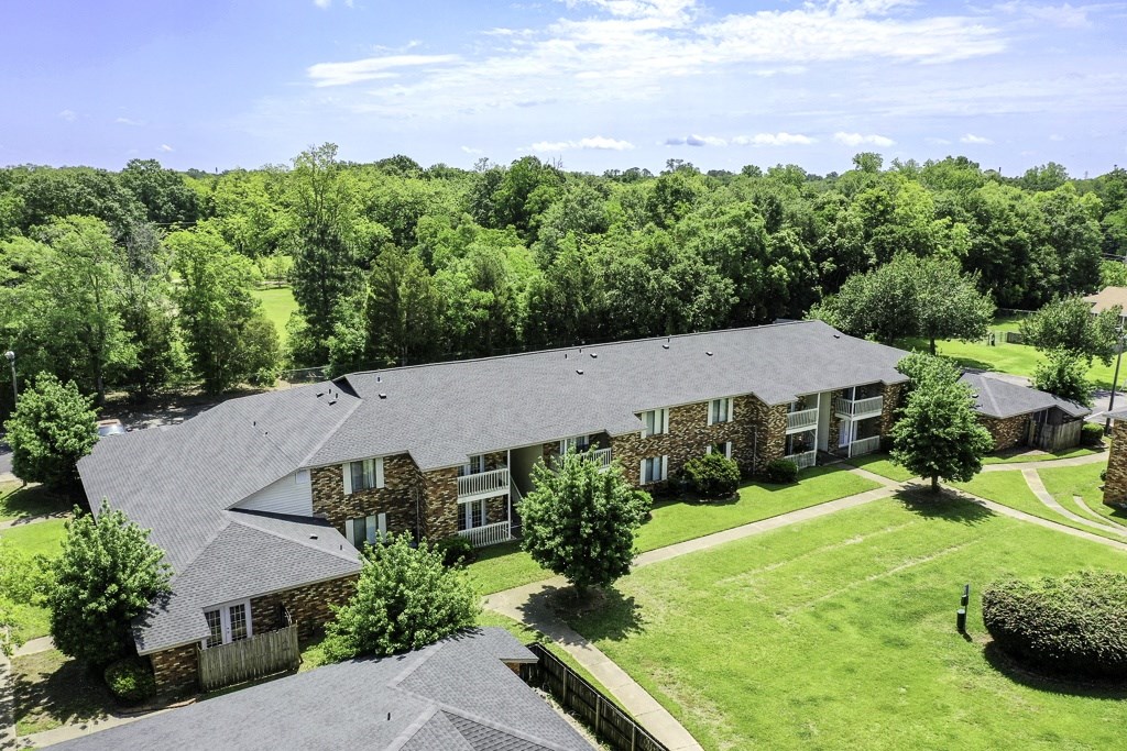A large house with a grey roof surrounded by a green lawn and trees.