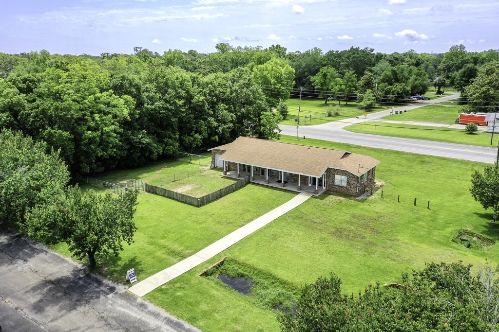 A house with a brown roof is surrounded by a green lawn and trees.