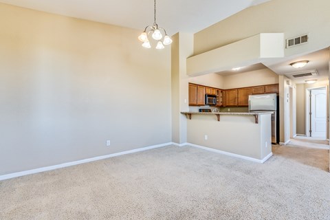 an empty living room with a kitchen in the corner