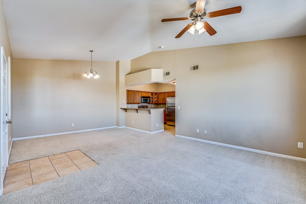 an empty living room with a ceiling fan and a kitchen
