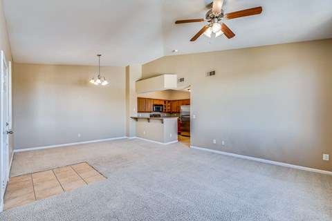 an empty living room with a ceiling fan and a kitchen