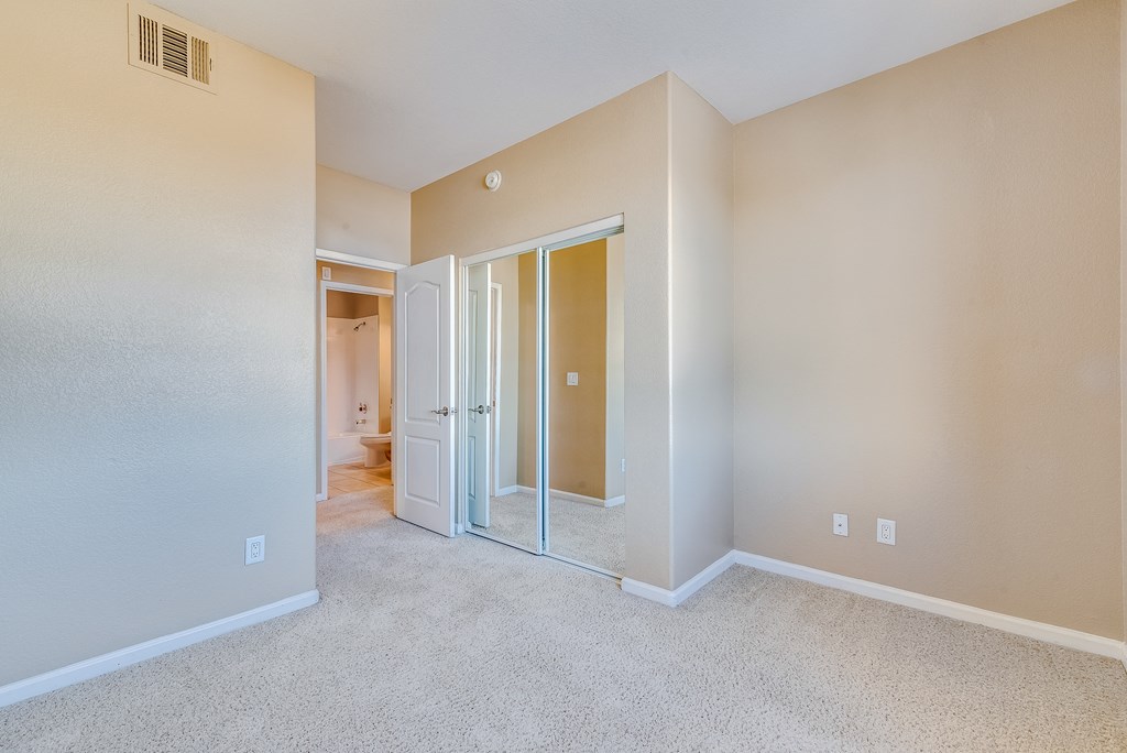 an empty bedroom with mirrored closet doors and carpeting