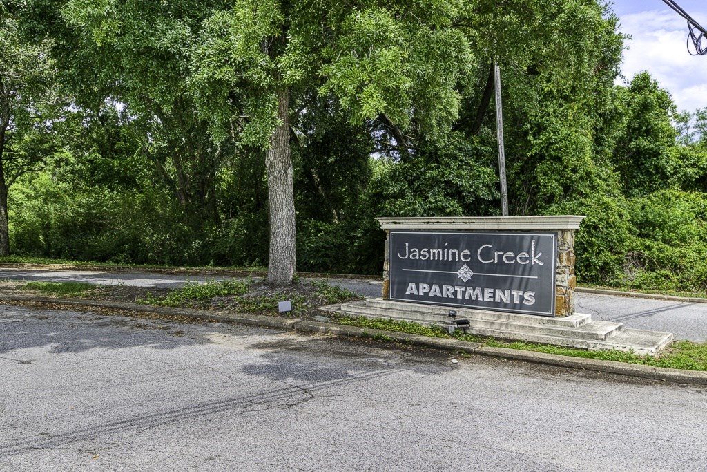 A sign for Jasmine Creek Apartments stands in front of a tree.