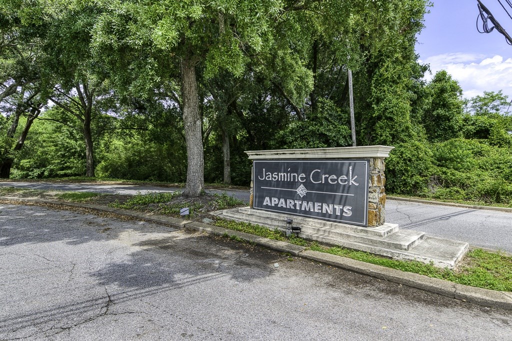 A sign for Jasmine Creek Apartments is displayed in front of a tree.