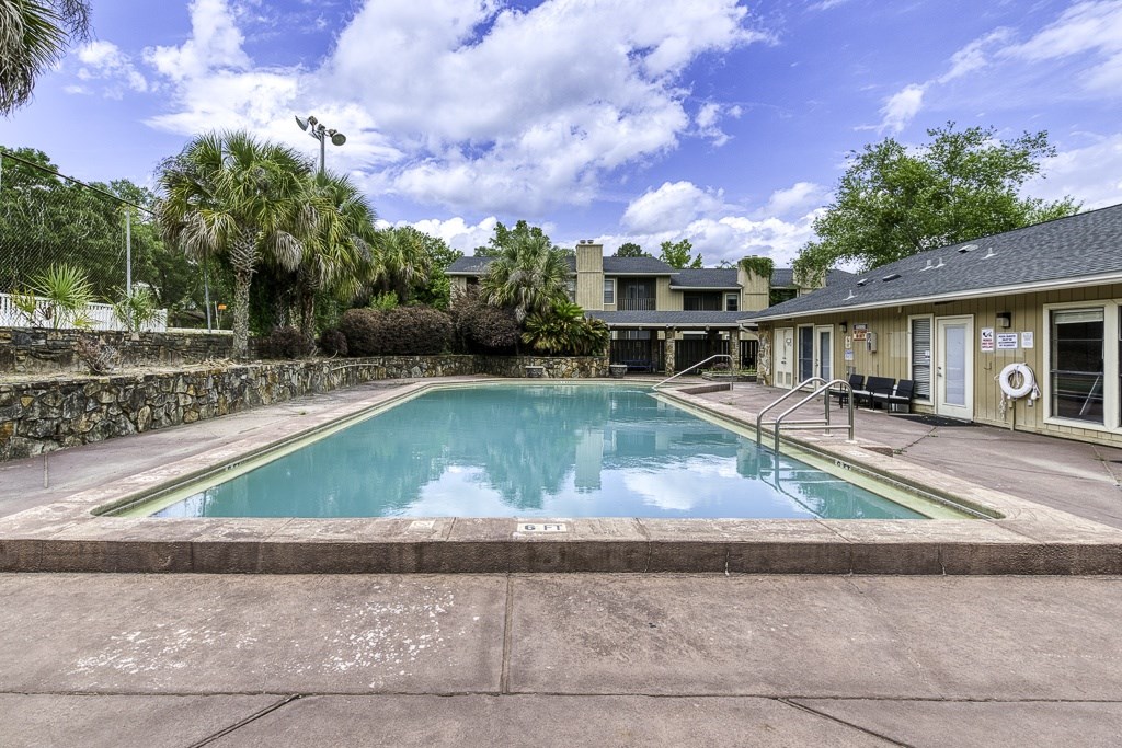A swimming pool surrounded by a stone wall and palm trees.