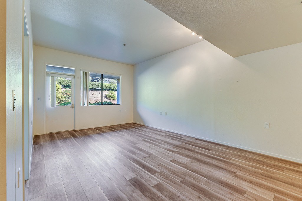A room with wooden flooring and a window with a view of a garden.