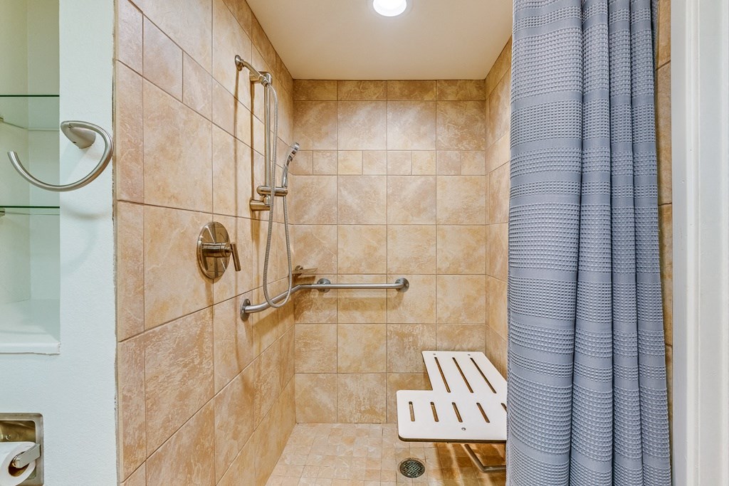A tiled shower with a bench and a shower head.