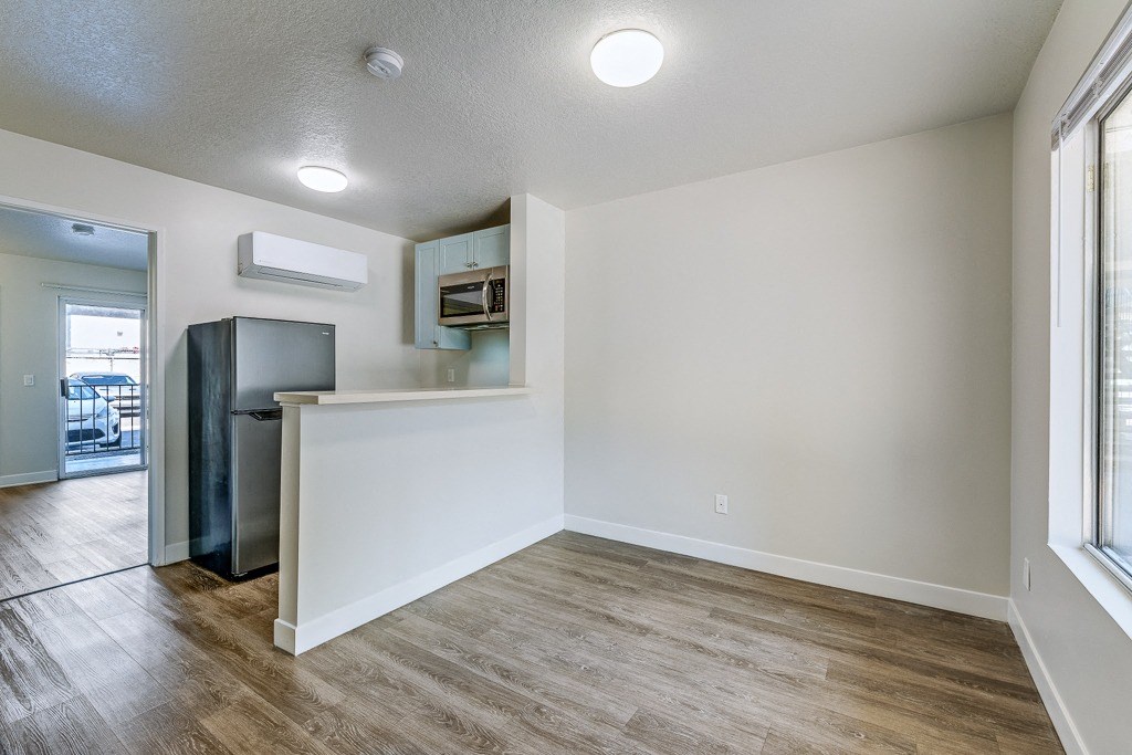 an empty living room with a kitchen and a refrigerator