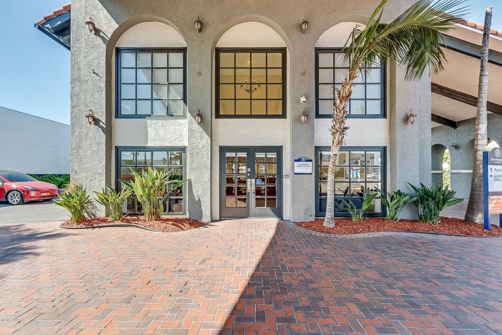 the front entrance of a building with a brick sidewalk and palm trees