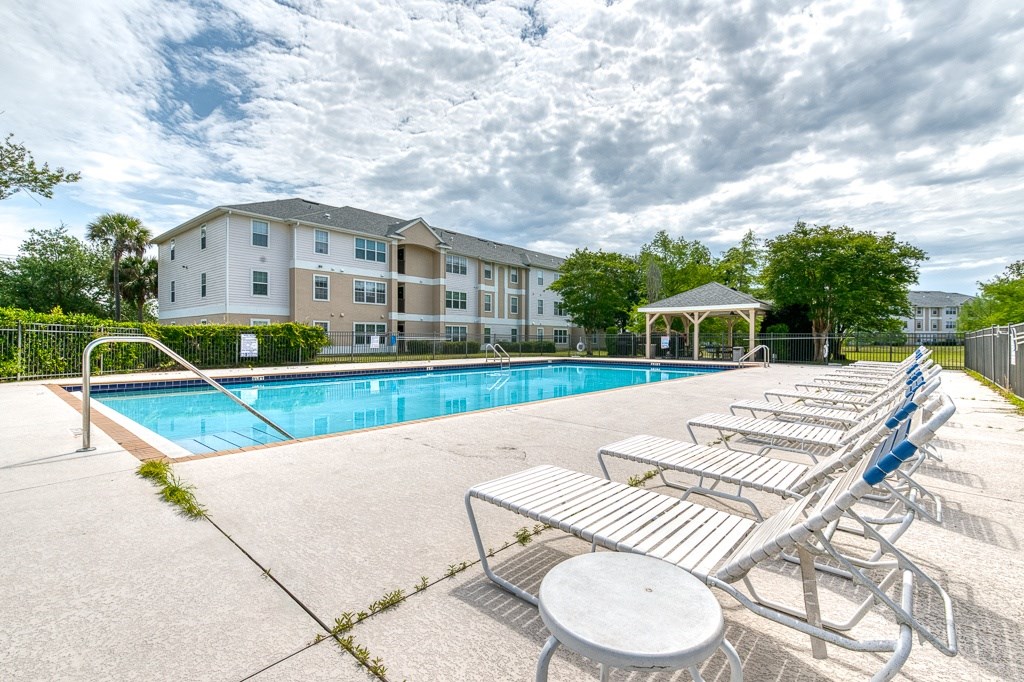A swimming pool with sun loungers and a building in the background.