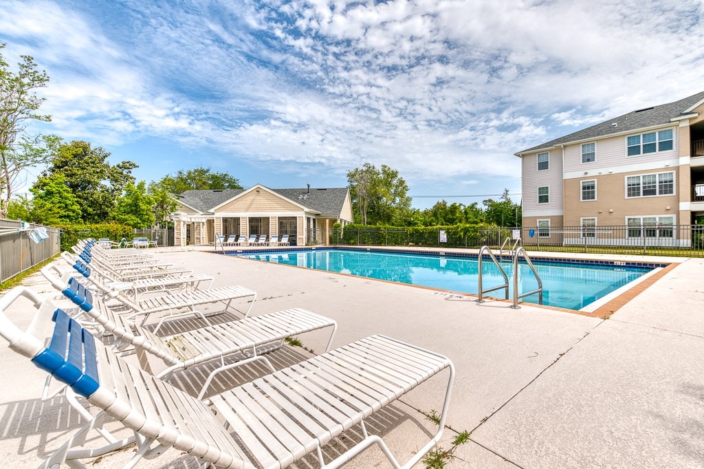 A pool area with sun loungers and a building in the background.