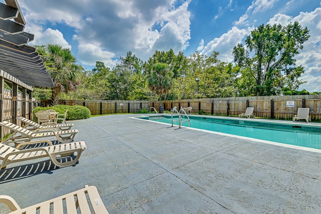 A pool surrounded by a wooden fence and multiple lounge chairs.