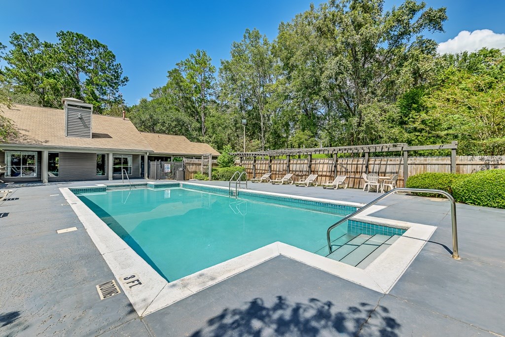 A swimming pool in a backyard with a house and trees in the background.