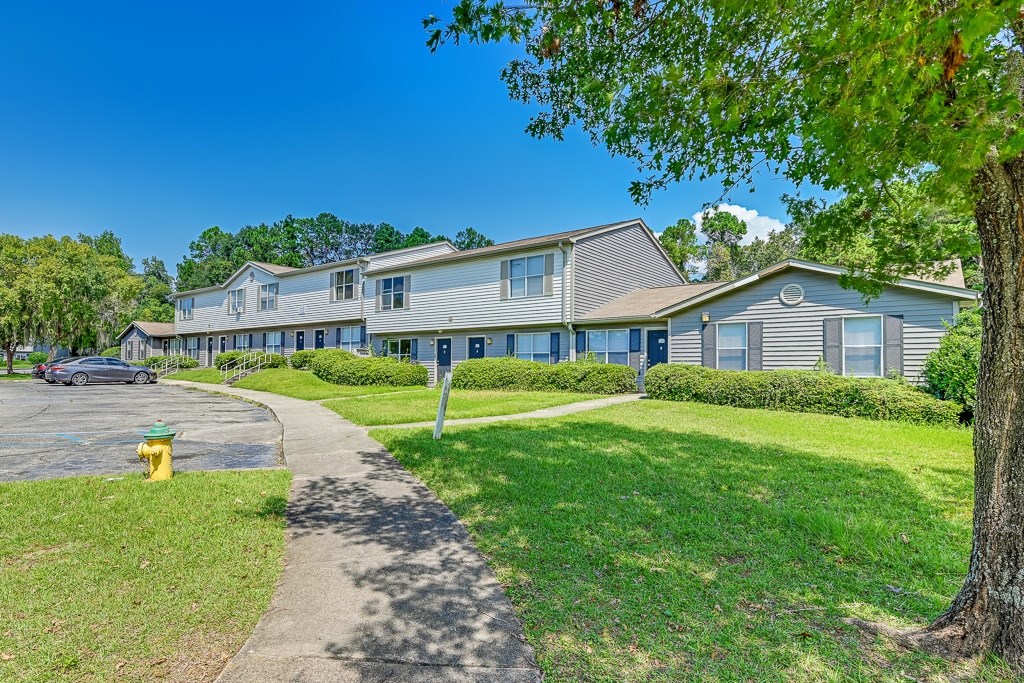 A yellow fire hydrant is on the left side of a grassy area in front of a building.
