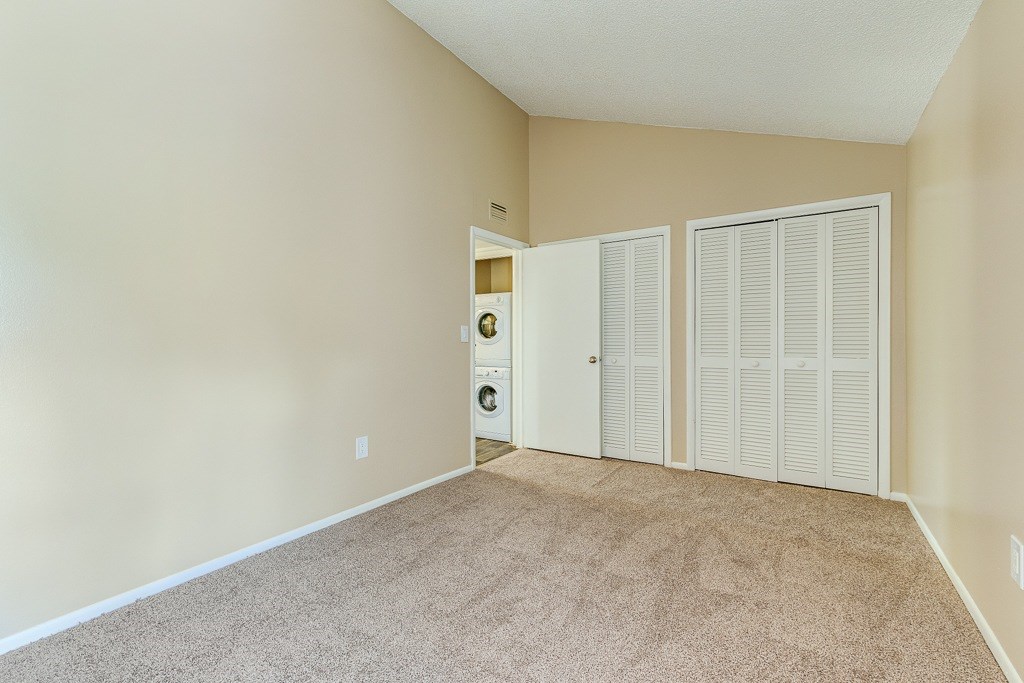 A room with a carpeted floor and a washer and dryer in the closet.