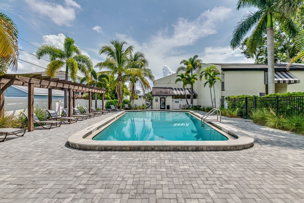 A swimming pool surrounded by palm trees and a brick patio.