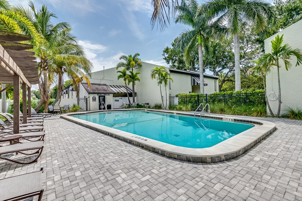 A swimming pool surrounded by palm trees and a brick patio.