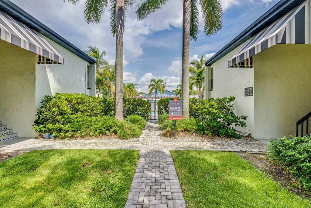 A sign in front of a building with a brick pathway leading to it.