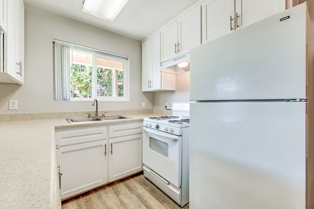 A white kitchen with a stove, sink, and refrigerator.