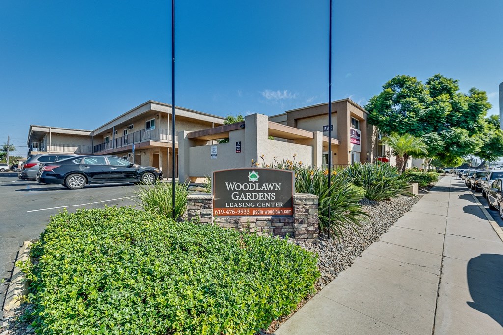 The image shows a leasing center named Woodlawn Gardens with a sign in front of it.