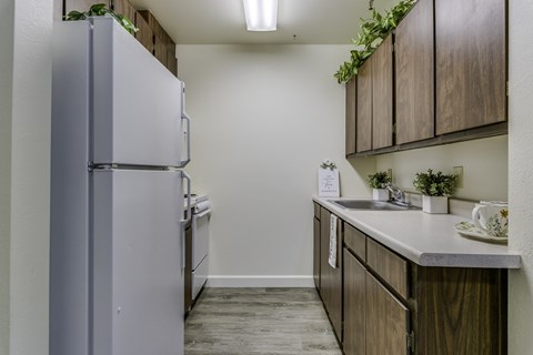 A kitchen with a refrigerator, wooden cabinets, and a counter with a sink.