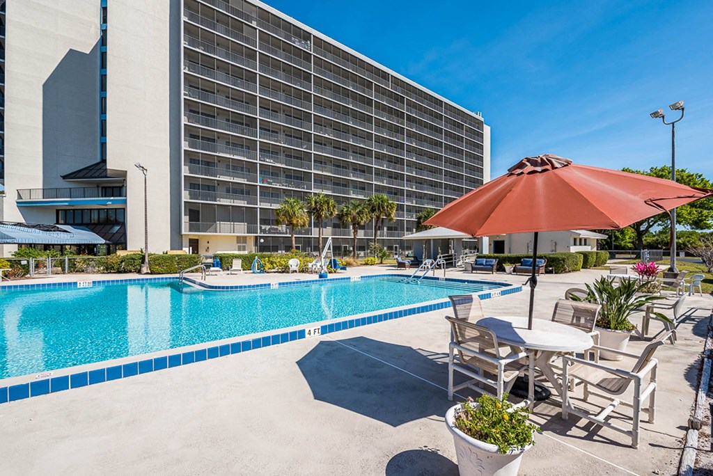 a swimming pool with a table and chairs and a hotel in the background