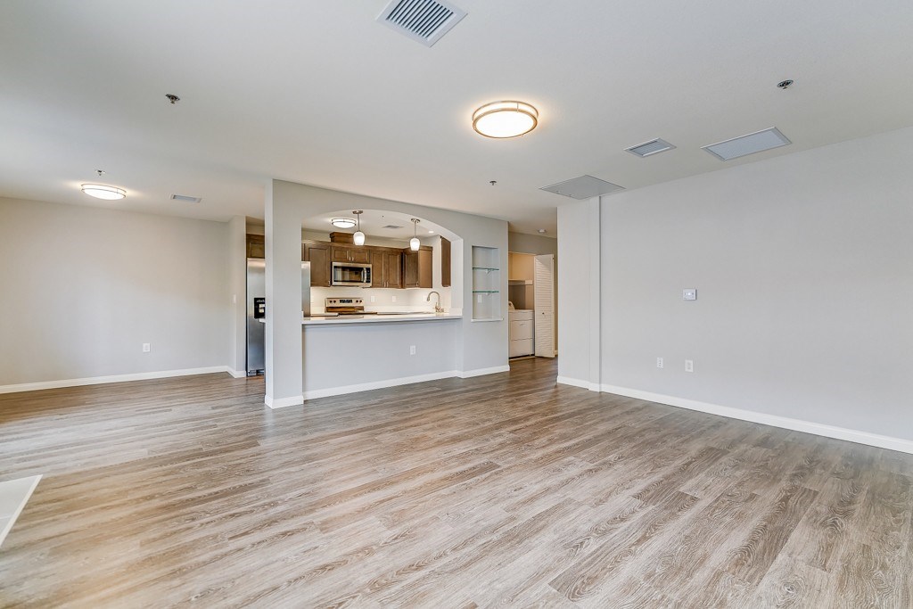 A spacious room with wooden flooring and a kitchen area in the background.