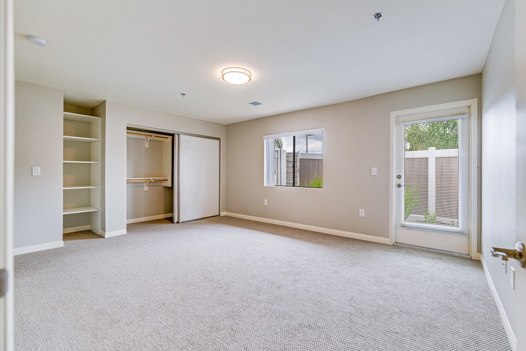 A spacious room with a carpeted floor and a window with blinds.