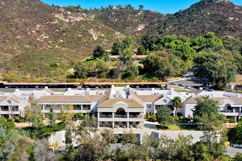 A large white building with a balcony is surrounded by trees and hills.