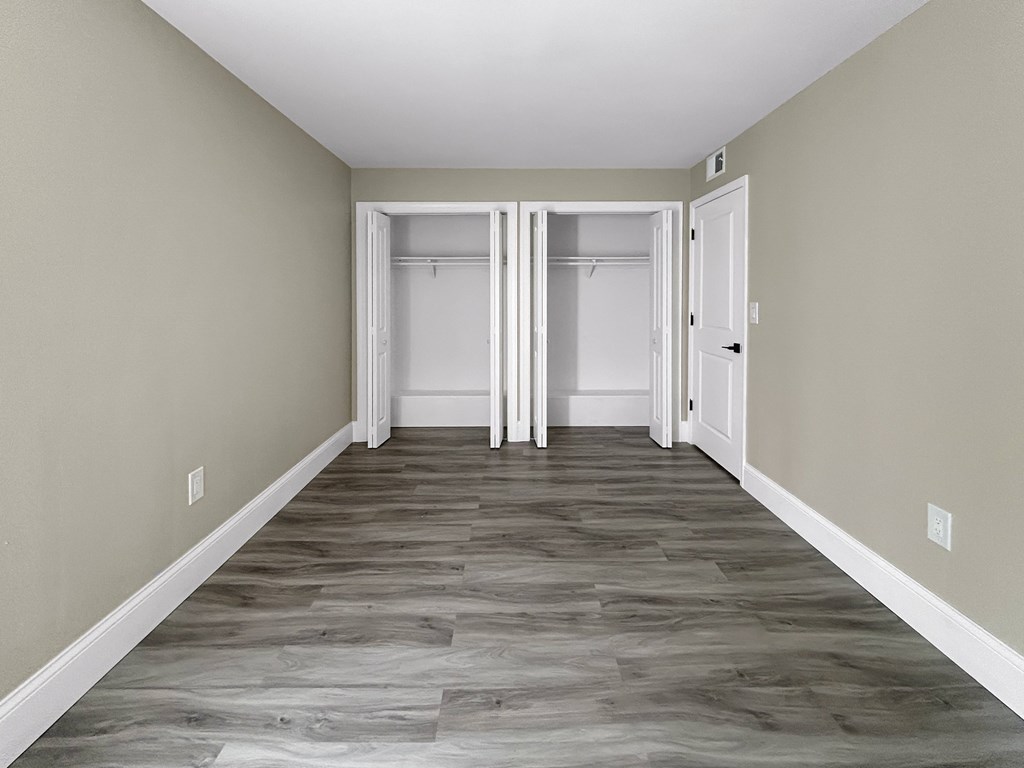 A long, empty hallway with white doors and wood flooring.