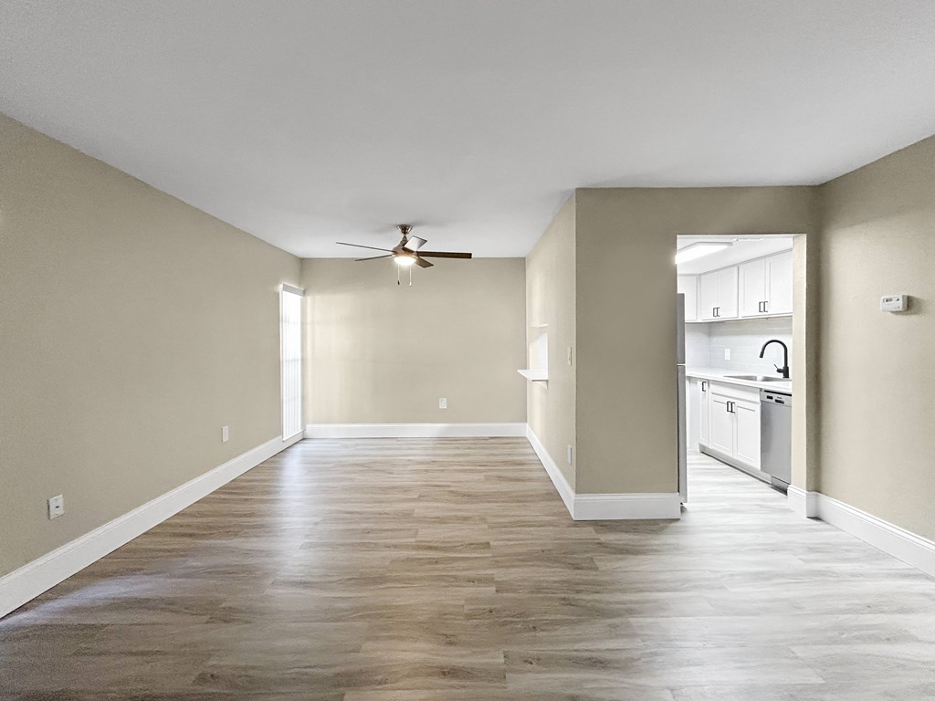 A spacious room with a ceiling fan and a kitchen area in the background.