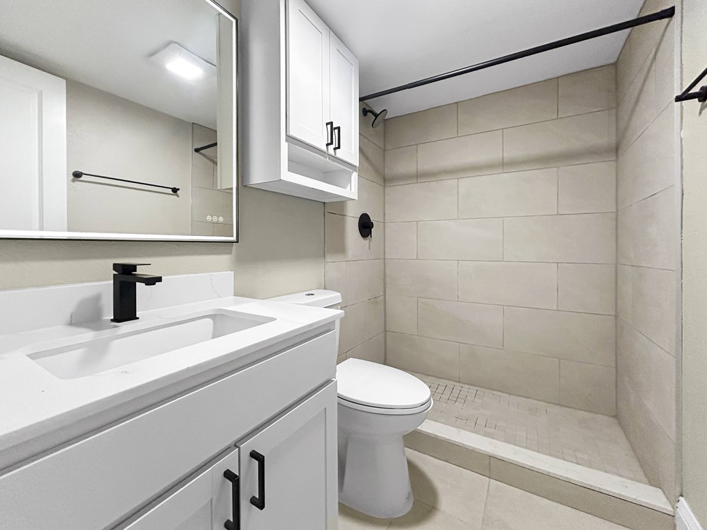 A white toilet sits in a bathroom with a white sink and a shower.