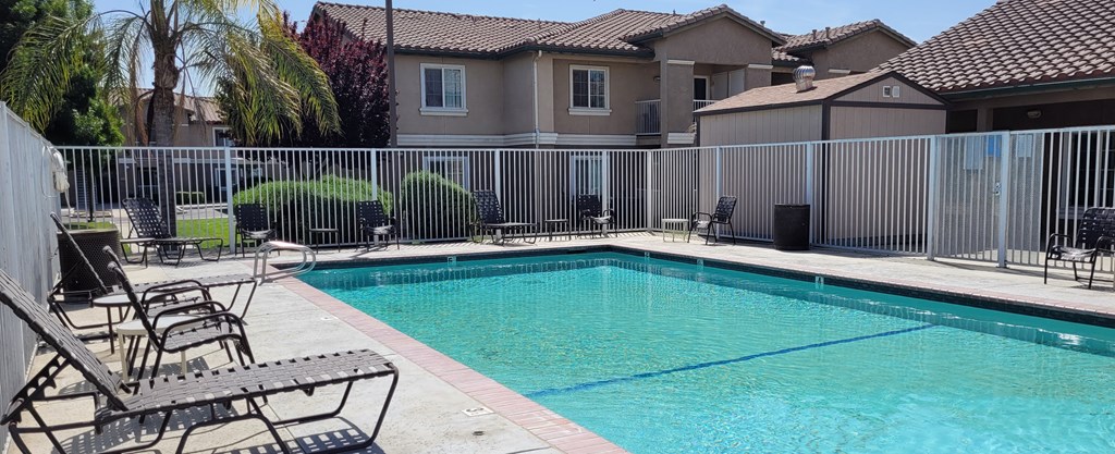 A pool surrounded by a fence with chairs around it.