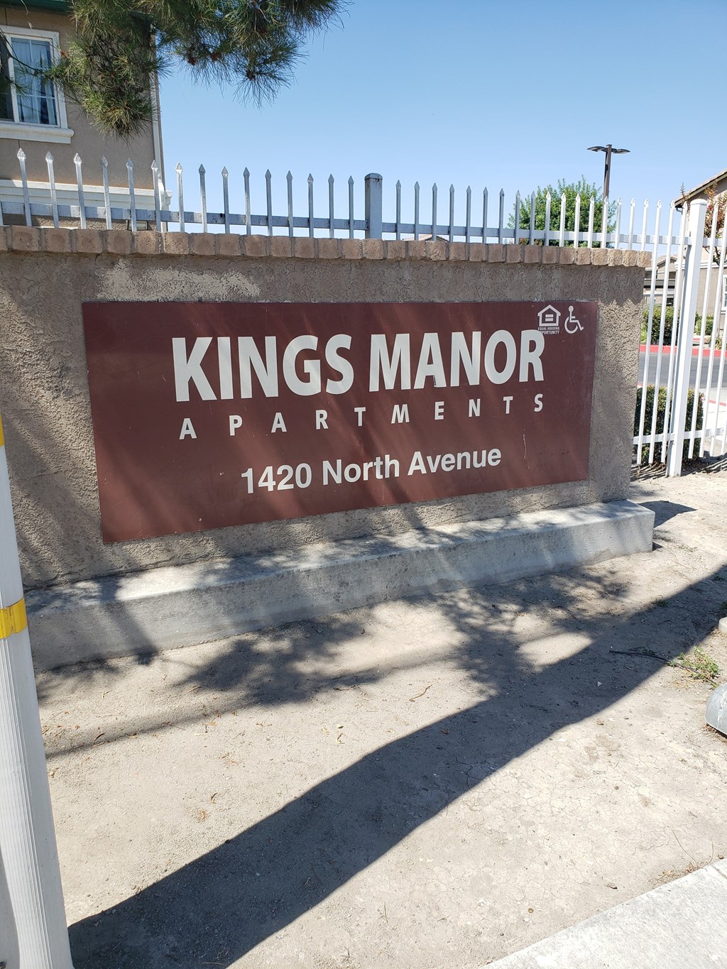 A brown sign that says Kings Manor Apartments stands on a sidewalk.