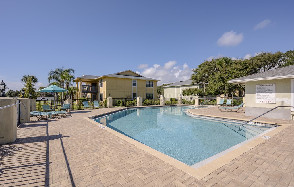 A pool surrounded by a brick patio and a white fence.