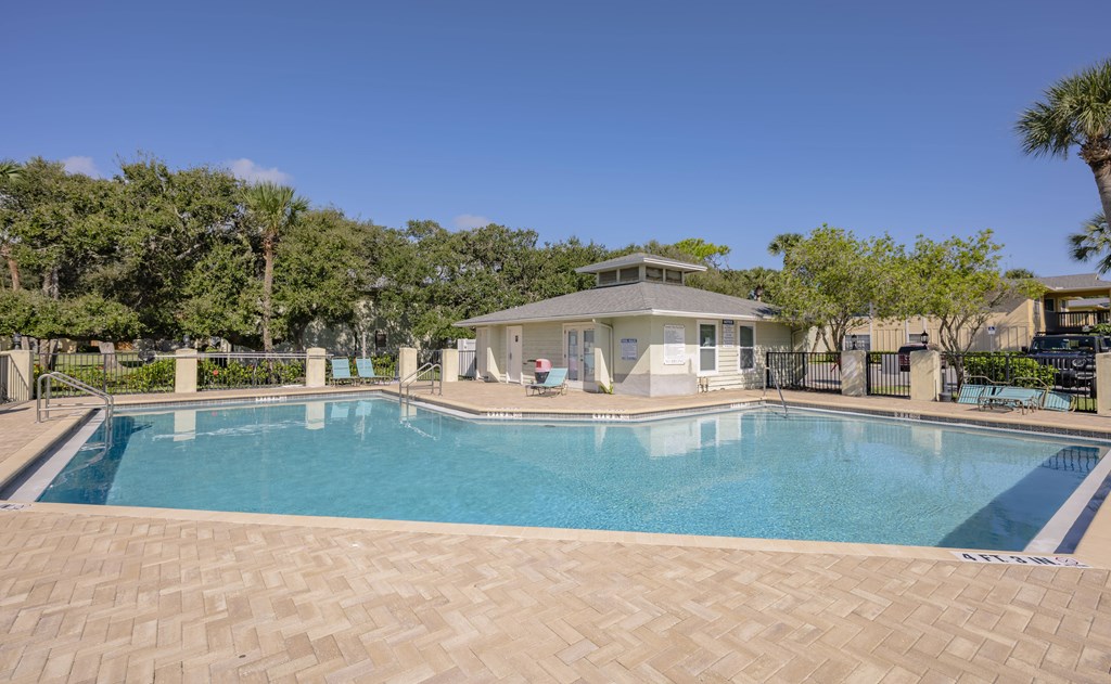 A large swimming pool surrounded by a brick patio and a house in the background.
