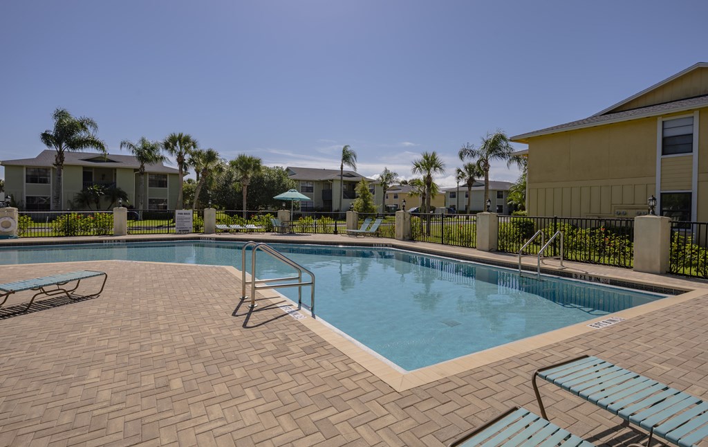 A swimming pool surrounded by lounge chairs and palm trees.