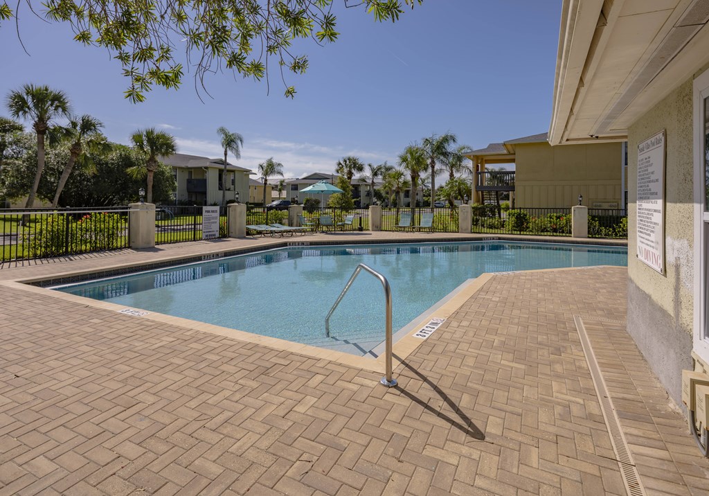 A pool surrounded by a brick patio and palm trees.