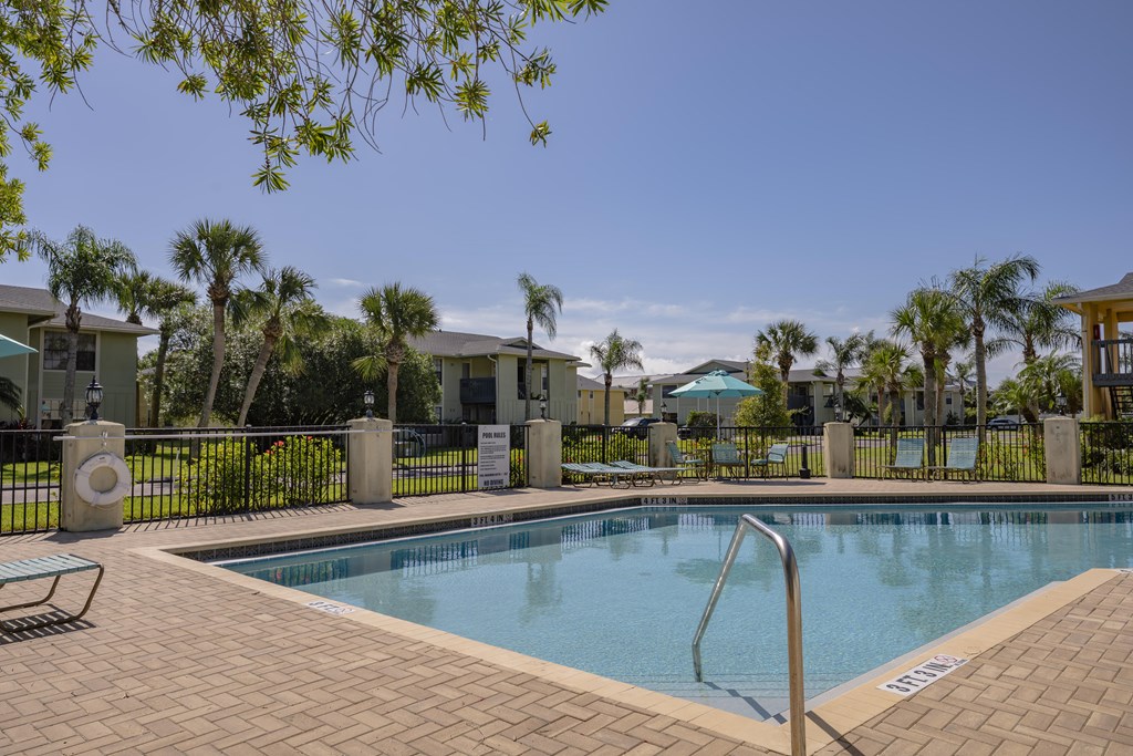 A swimming pool surrounded by a brick patio and palm trees.