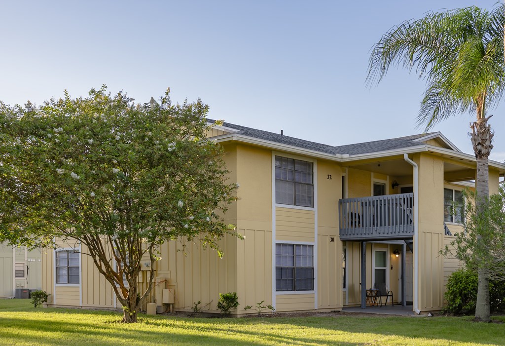 A yellow building with a balcony and a tree in front.