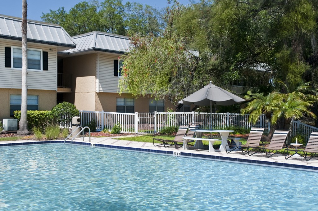 a swimming pool with chairs and a umbrella in front of a house