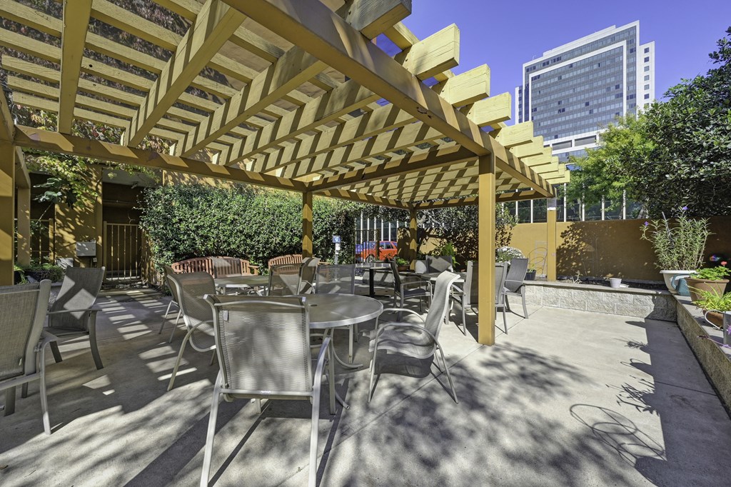 a patio with tables and chairs under a wooden pergola at The Riverview (55+), Sacramento, CA