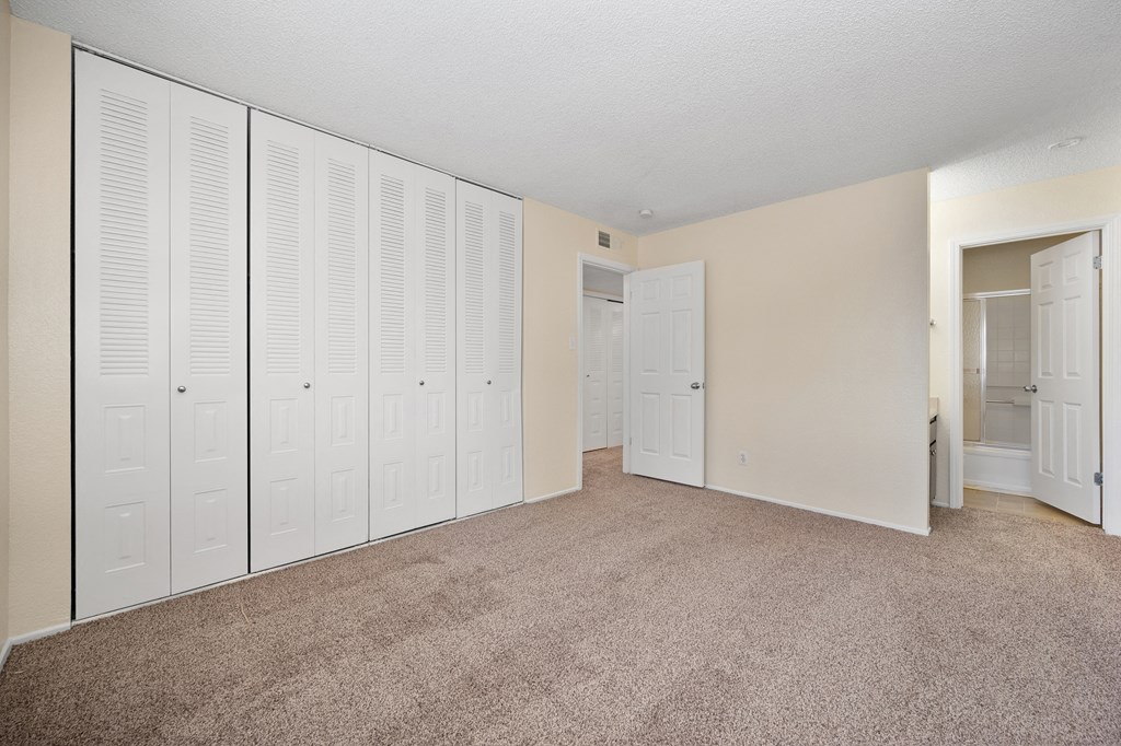 an empty bedroom with white closet doors and carpeting