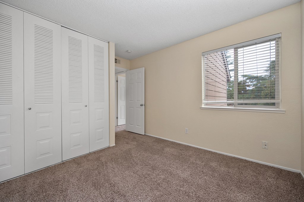 an empty bedroom with white closet doors and a window