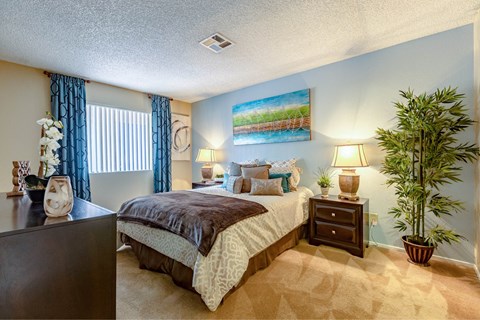 A bedroom with a bed, nightstand, and a potted plant.